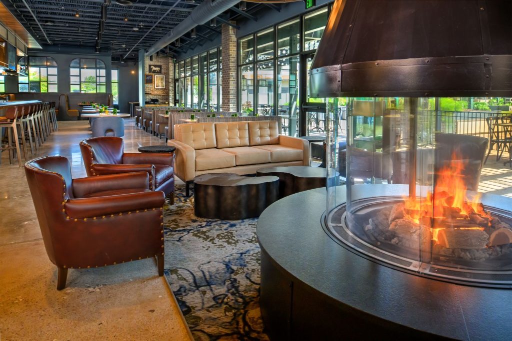 A cozy fireplace in Basso Westport restaurant, surrounded by tables and chairs for dining guests.